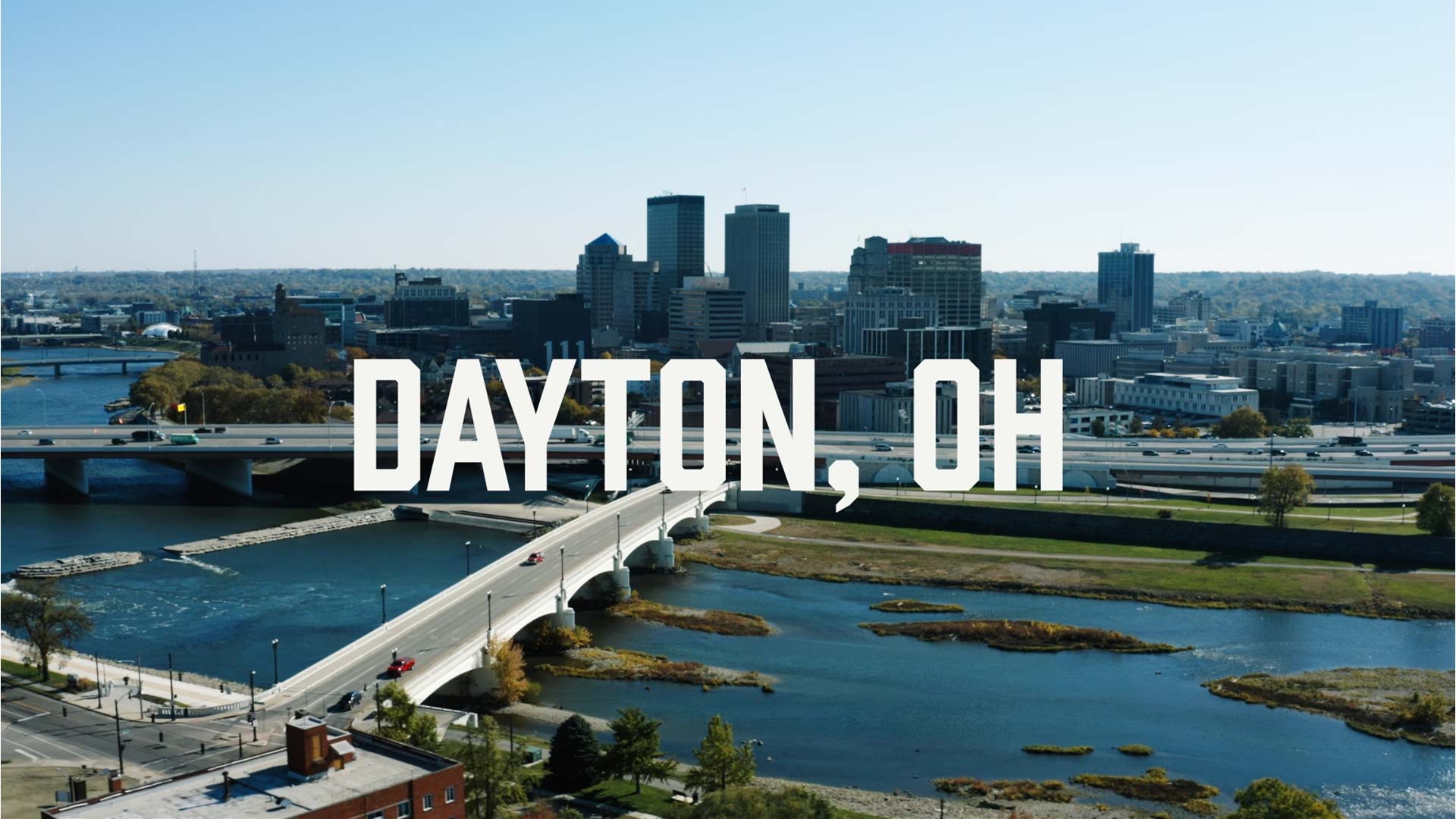 A city skyline of Dayton, Ohio, with tall buildings, a river, bridges, and DAYTON, OH written in bold white text across the center. The scene hints at local favorites like Belle of Dayton Distillery and Crafted & Cured—spotlighting the city’s vibrant downtown spirit.